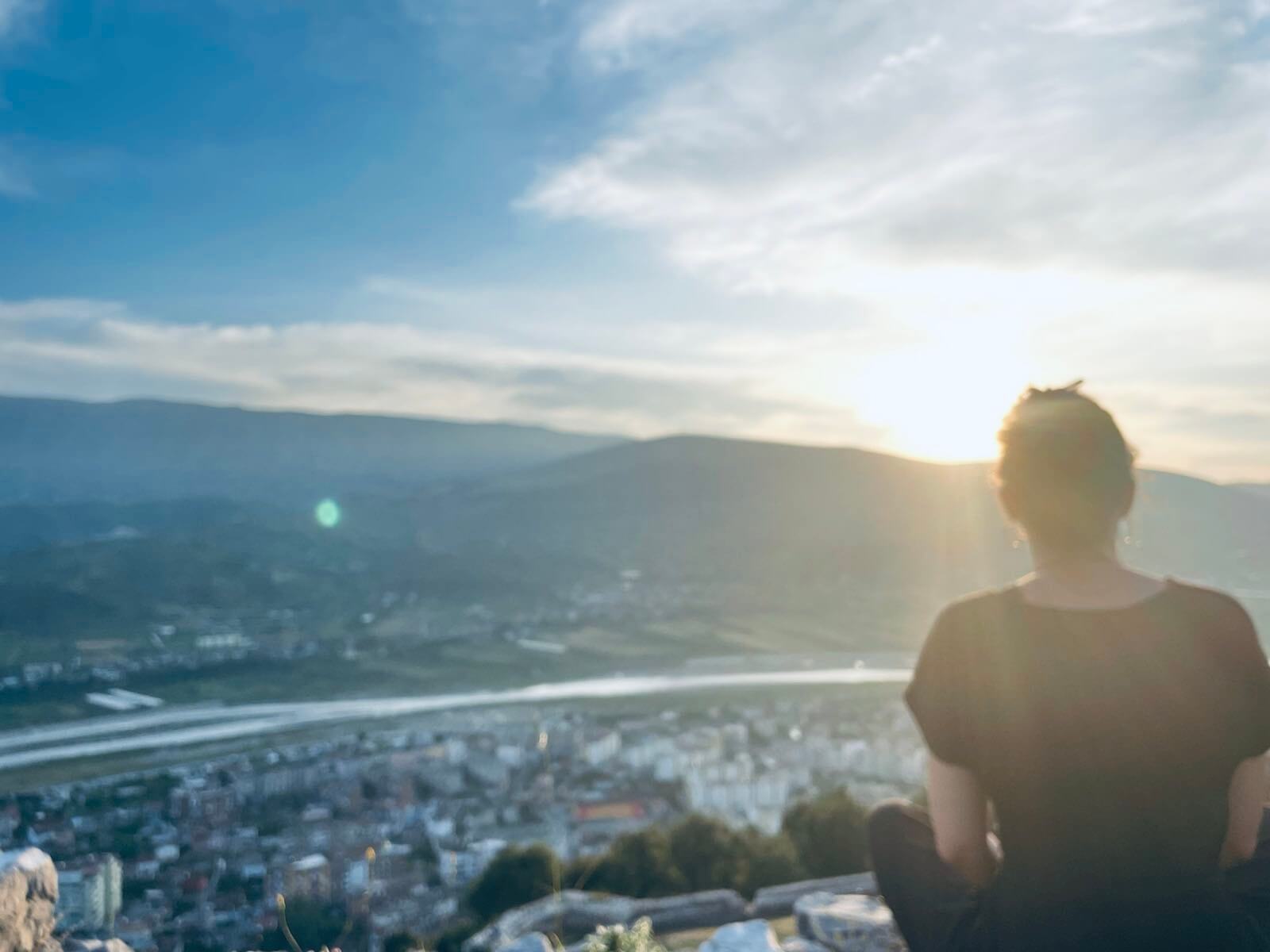 Der Texter Gesundheit sitzt in der Abendsonne auf einem Berg und schaut über das Tal. 