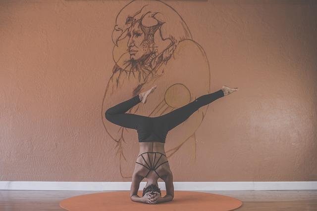 Eine Frau in Yogapose von hinten. Sie macht einen schwierigen Kopfstand. An der Wand eine Zeichnung einer Frau.