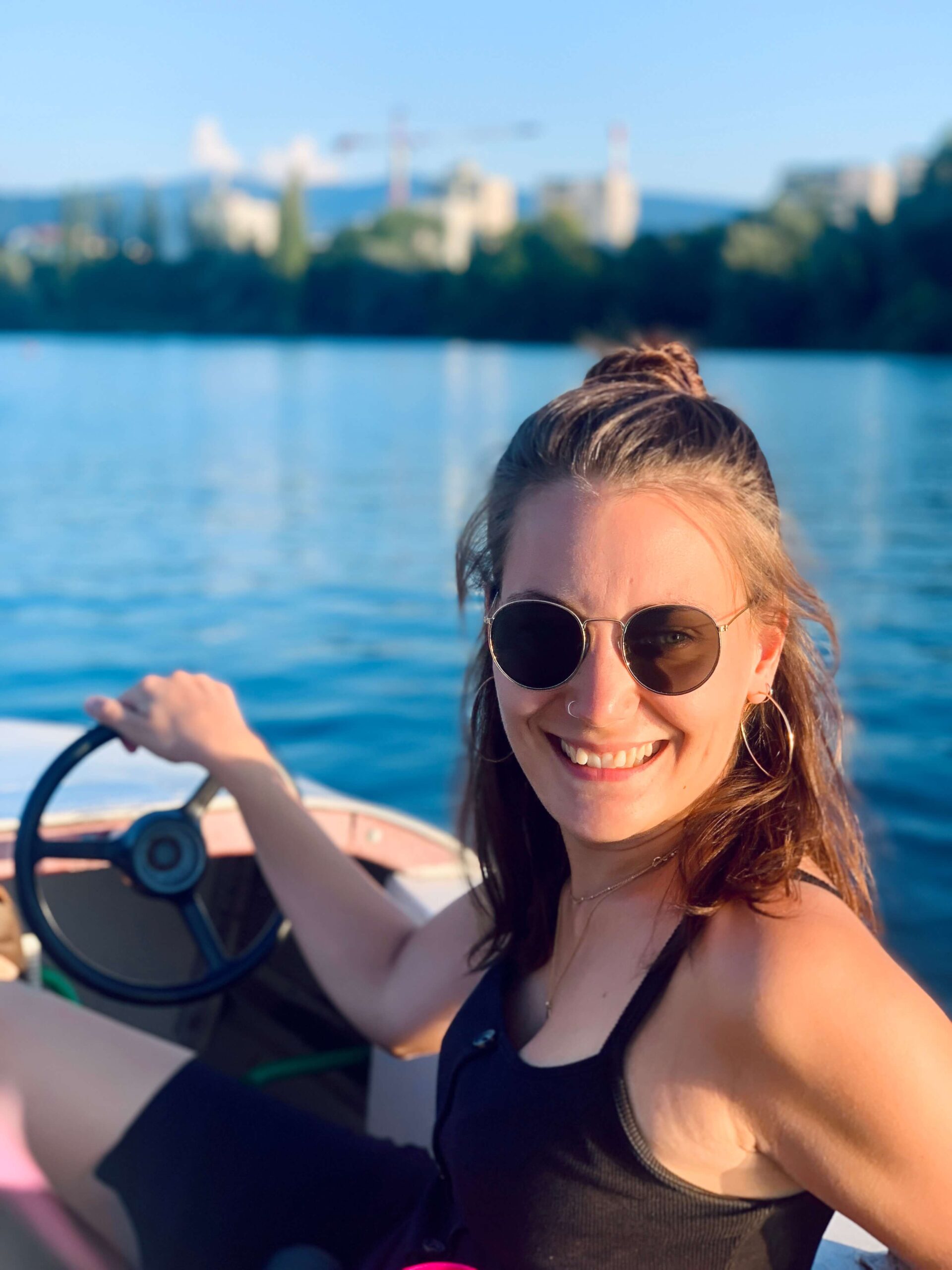 Texterin Liliane Herzberg sitzt in einem Tretboot am Lenkrad und lächelt in die Kamera. Sie trägt eine Sonnenbrille. 