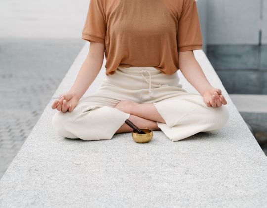 Eine Person im Yoga-Schneidersitz. Sie ist zur Hälfte zu sehen. Vor ihr eine Klangschale. 