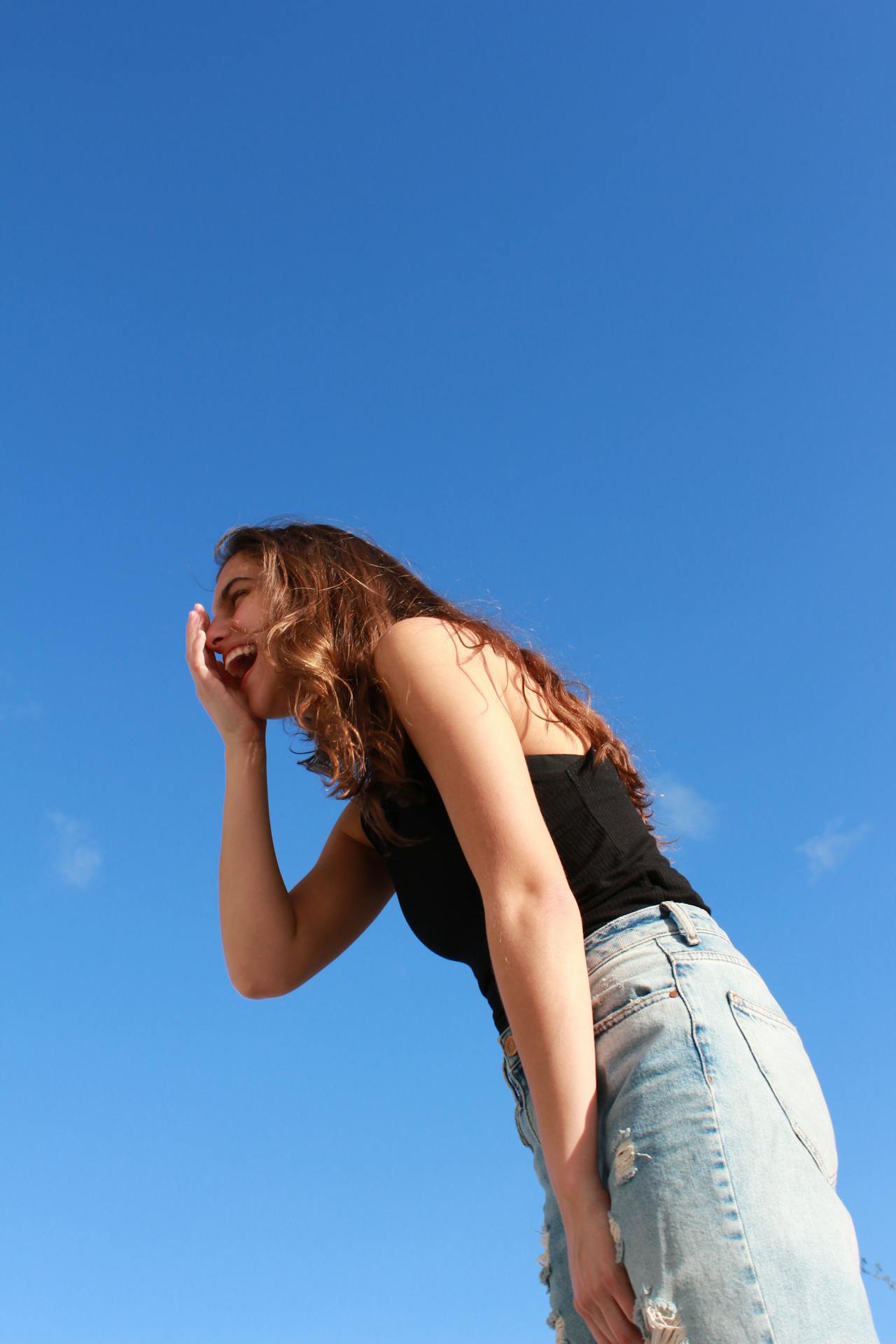 Eine junge Frau vor blauem Himmel jauchzt vor Freude, weil sie ihre Blogartikel schreiben lassen hat.