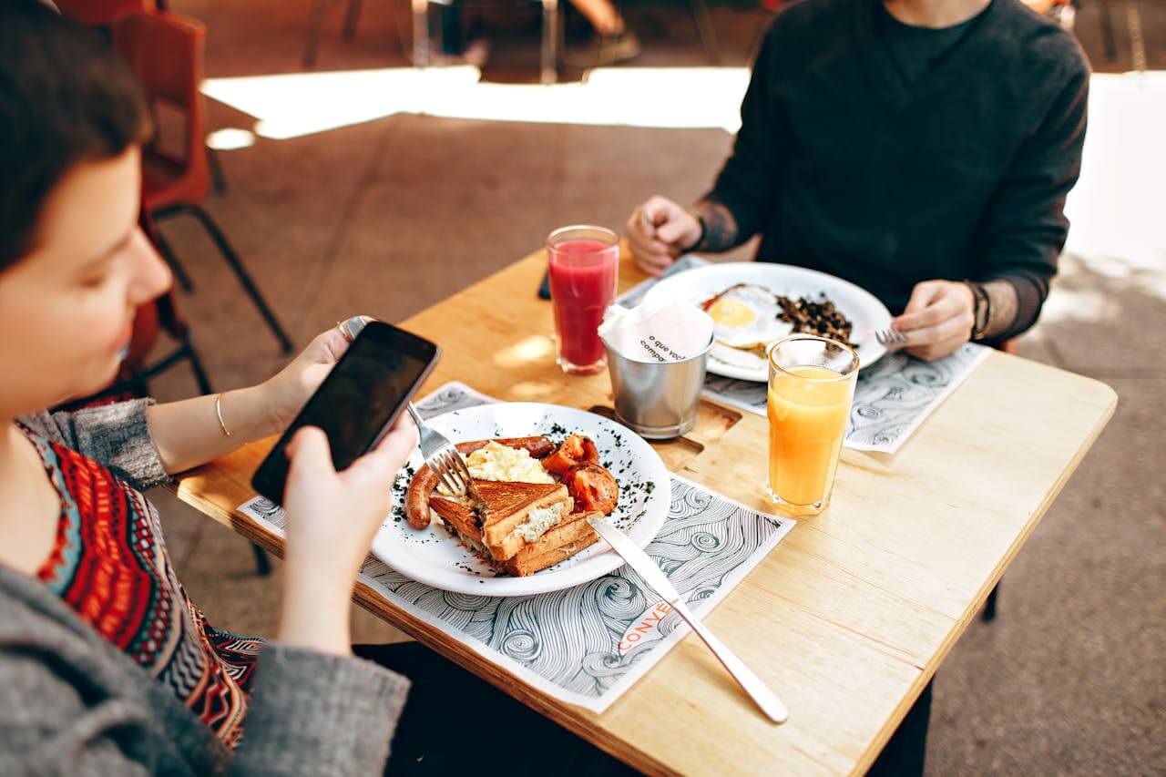 Zwei Mädchen am Frühstückstisch. Eine sitzt am Handy und liest die SEO Tipps für Anfänger.