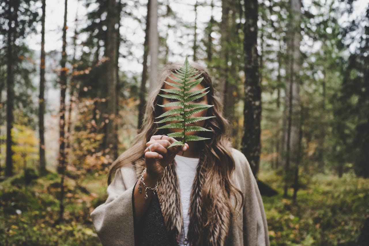 Eine Frau steht im Wald, sie hält sich ein Farn vor das Gesicht. Sprüche Achtsamkeit kennt sie vielleicht?