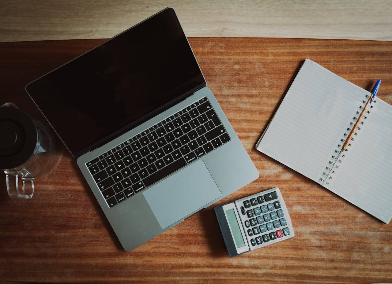 Ein Laptop, ein Block, ein Taschenrechner auf dem Schreibtisch. Wie hoch ist der Texter Preis?