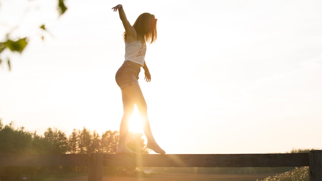 Eine Frau spaziert über einen querliegenden Baumstumpf. Es ist nur ihre Silhouette im Abendlicht zu sehen. Sie kümmert sich um ein achtsames Leben.